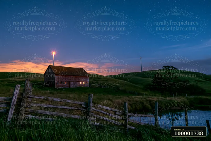 A wind turbine stands tall against a starry night sky over a rural setting.