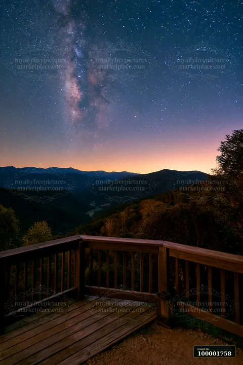 The view shows a starry night above a mountain valley, with a wooden deck in the foreground.
