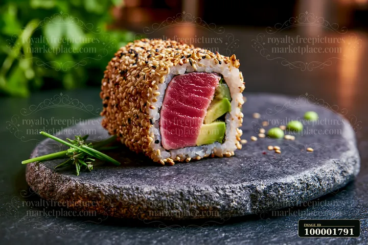 One tuna roll slice with sesame coating rests on a dark stone plate.