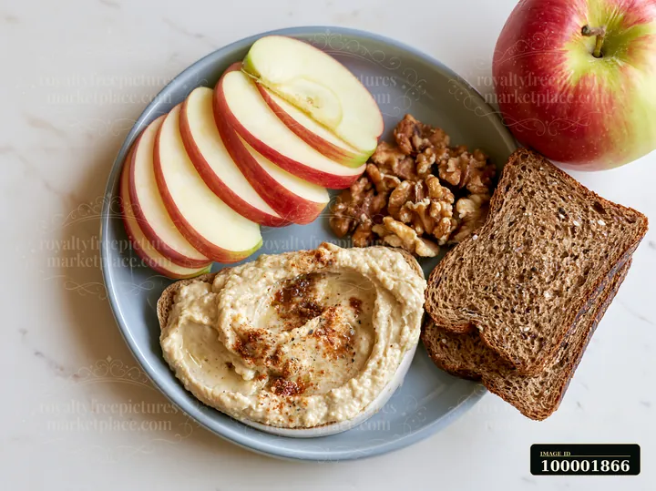 A breakfast plate features hummus, sliced apples, walnuts, and whole grain bread.