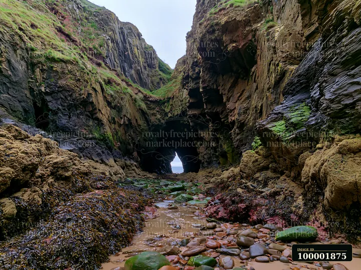A rocky coastline beneath dramatic cliffs features a cave entrance that opens to the sea.