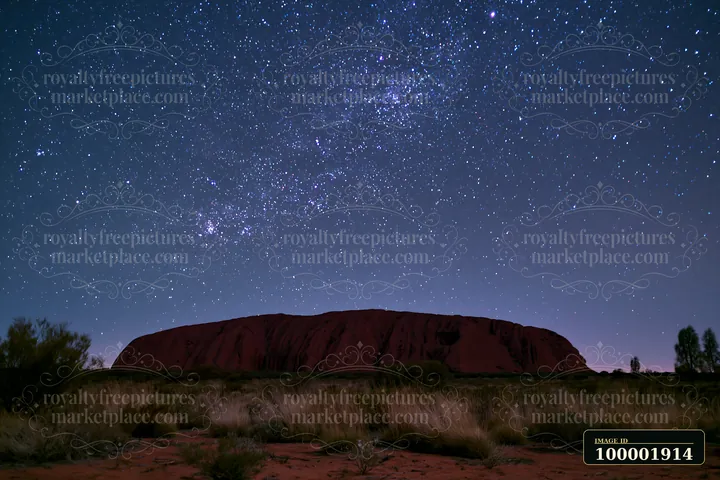 Uluru stands prominently under a starry night sky, showcasing a vast expanse of stars.