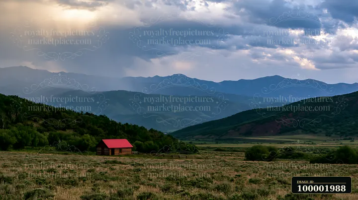 A cabin sits in the foreground as dark thunderstorm clouds gather over a mountain range in the background.