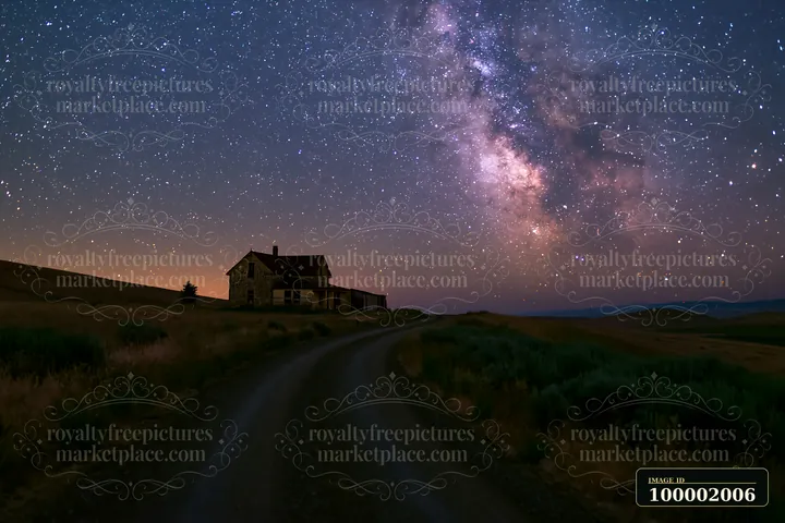A remote house stands alone on a dirt road with the Milky Way shining brightly above it in the night sky.