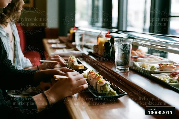 Two people enjoy a romantic sushi dinner at a wooden table by a window.