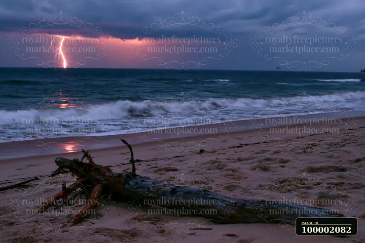 Lightning strikes over the ocean near a sandy coastline with waves hitting the shore.