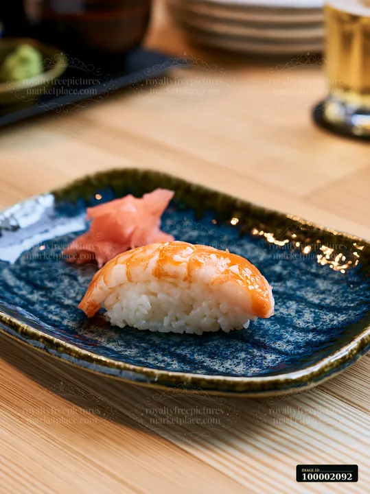 One sushi piece with pickled ginger sits on a blue plate.