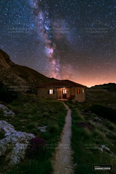 A remote house stands under the Milky Way, illuminated by its windows.