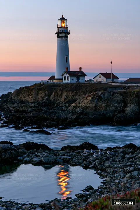 The lighthouse near a rocky tide pool stands tall against the evening sky.