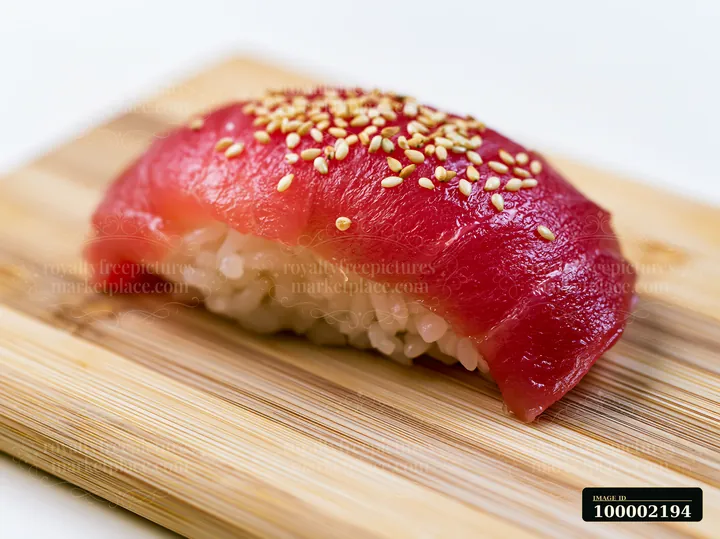Single tuna nigiri on wooden board shows a piece of sushi topped with fresh tuna and sprinkled with sesame seeds.