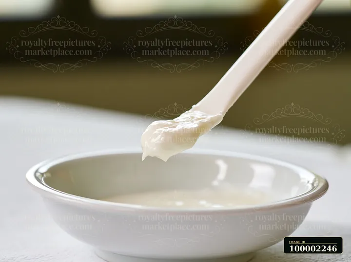 A cosmetic spatula holds a dose of cream above a white bowl.
