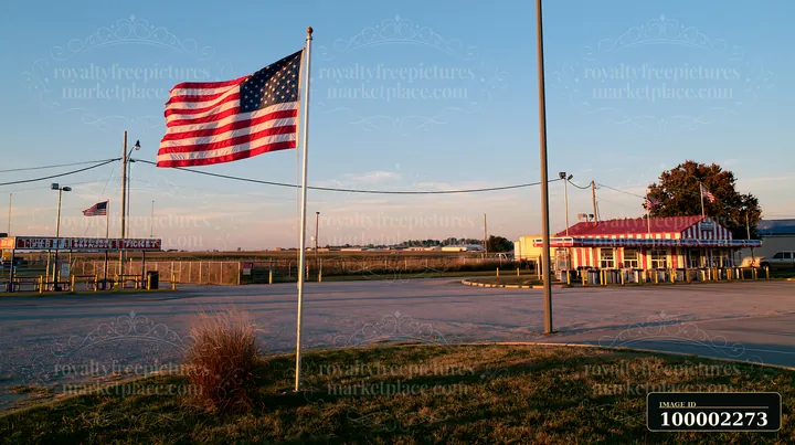 An American flag flying in strong wind stands prominently near a roadside stand.