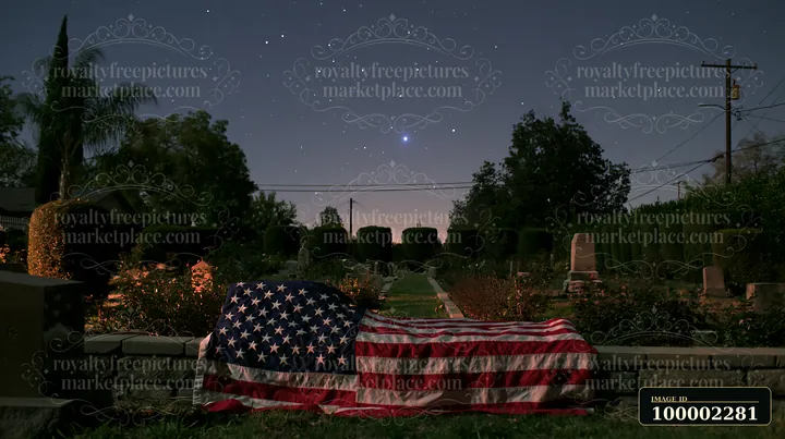 A solemn cemetery scene with American flag and stars shows a flag placed on a grave in a well-maintained cemetery.