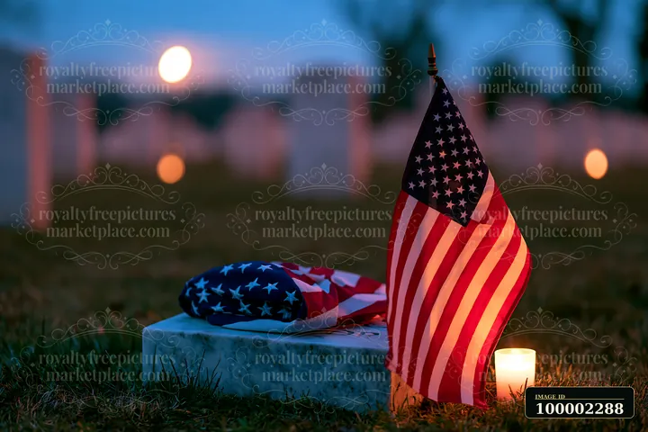 Flags and a candle are positioned at a grave in a veterans cemetery under a clear night sky.