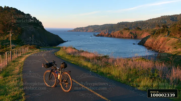 A bicycle is parked along a road that runs through a coastline with sheltered bay at sunset.
