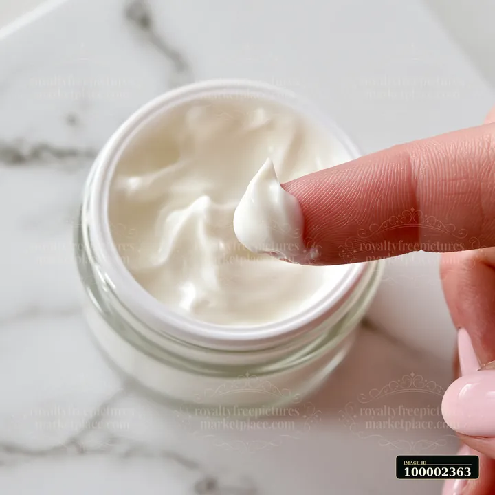 A close-up shows a finger dipping into a jar of cream on a marble surface.