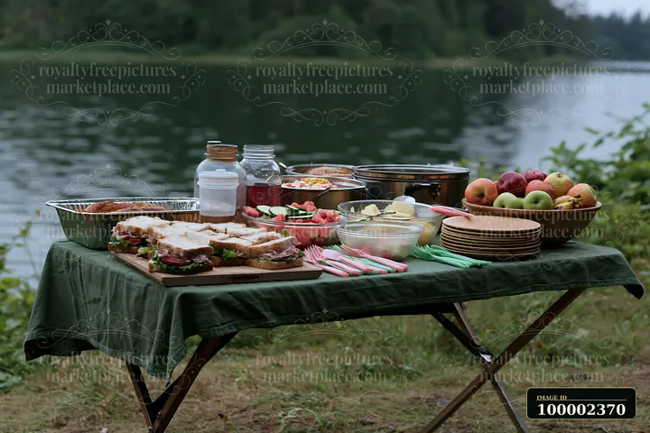 A zero waste buffet table is set up near a lake, featuring sandwiches, fruits, and various dishes.