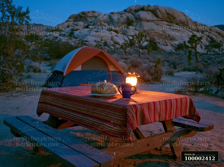 A table is set with bread and a mug beside a lantern at a campsite under a starry night sky.