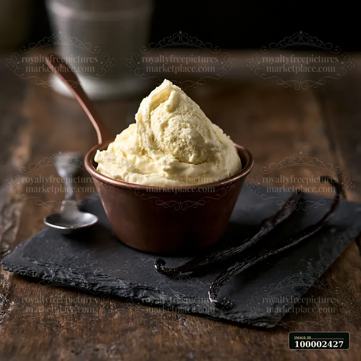 A bowl of cream sits on a dark stone surface, accompanied by vanilla pods.