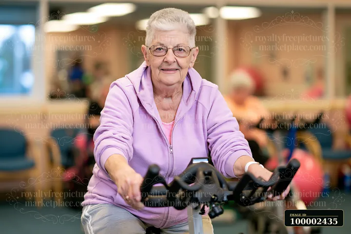 A senior with Parkinson's using a stationary bicycle is exercising in a gym.