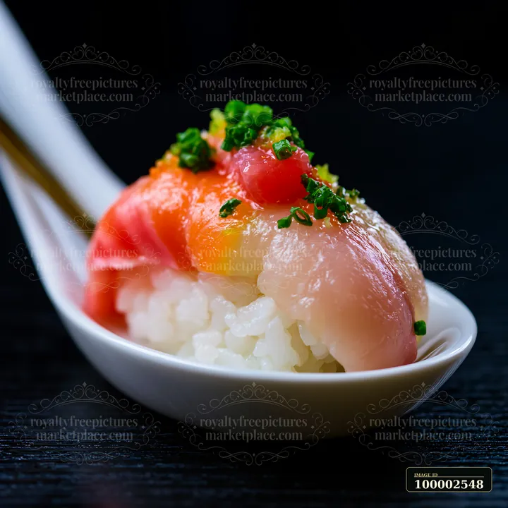 A single sushi piece with colorful fish topping is placed on a white spoon against a dark background.