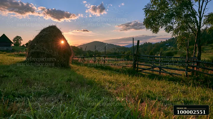 A traditional haystack sits in a meadow as the sun sets behind rolling hills.