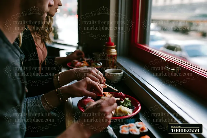 Two people enjoy a romantic sushi dinner while seated at a window table.