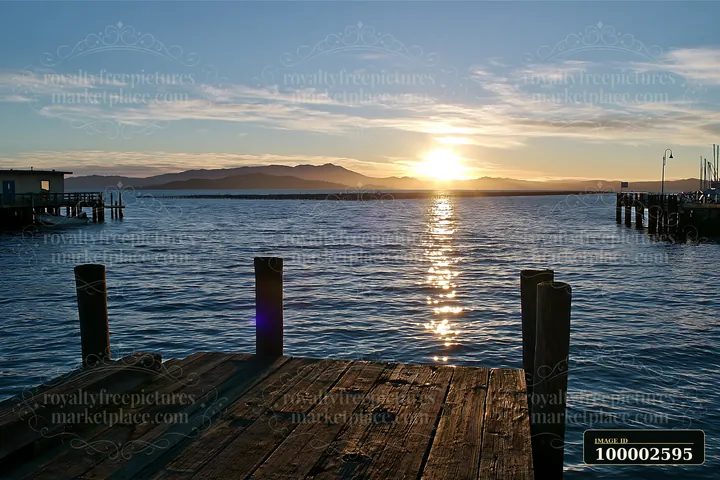 Sunset over a coastline with mussel farms, casting golden reflections on water.