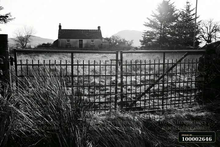 A rural cottage is visible through a metal gate in a field.