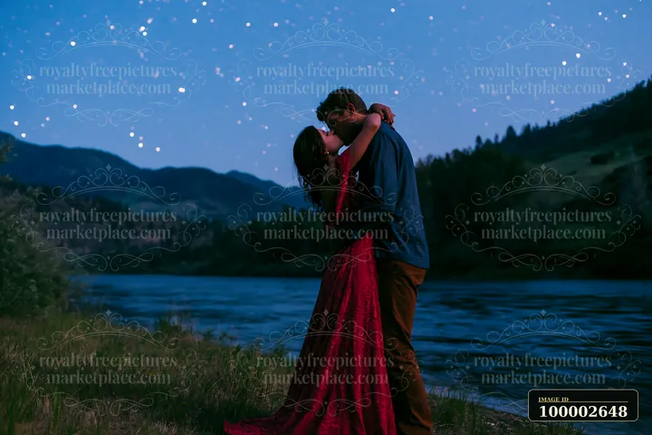 A happy couple kissing beneath stars in nature by a river.