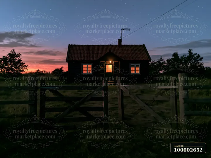 A small house stands in a meadow, illuminated by lights from its windows.