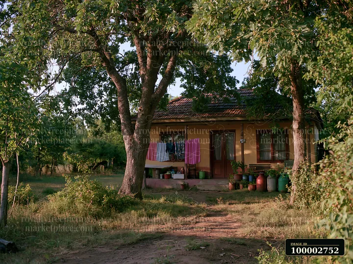 A rural home under oak trees features a porch with laundry hanging to dry.