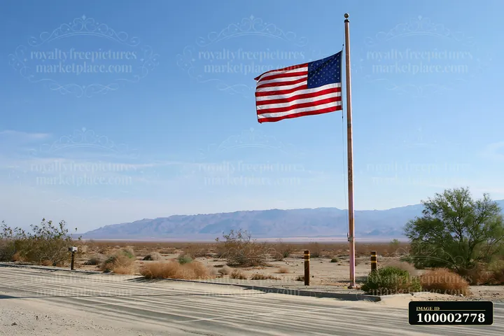 An American flag flying in strong wind stands tall on a flagpole against a clear sky.