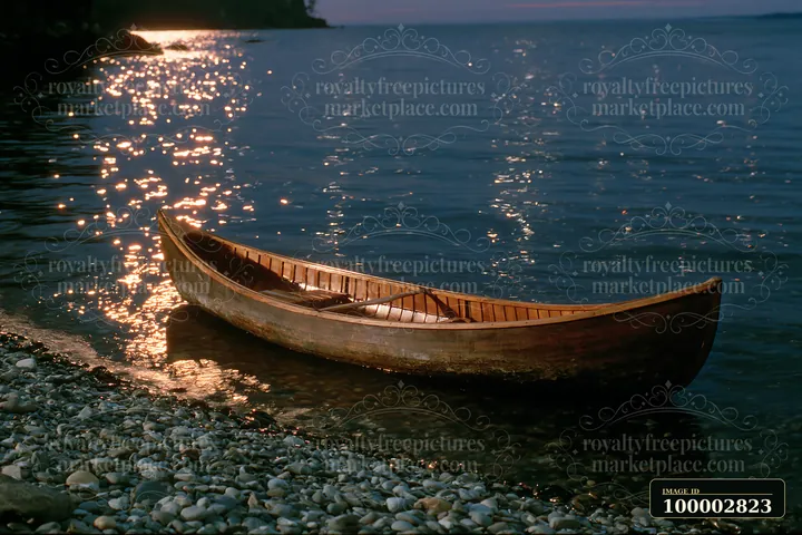 A canoe rests on pebbles by the water as stars shine brightly in the night sky.