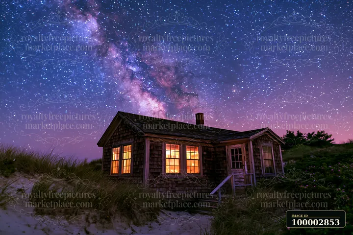 A beach house sits under a clear night sky filled with stars, with the Milky Way visible above.