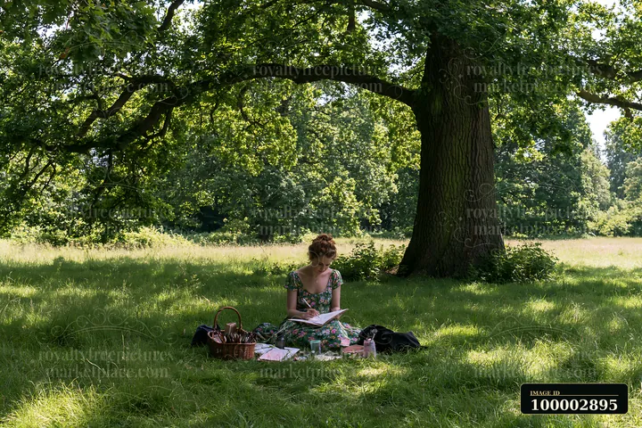 A woman sits on the grass in a meadow, sketching with tools nearby.