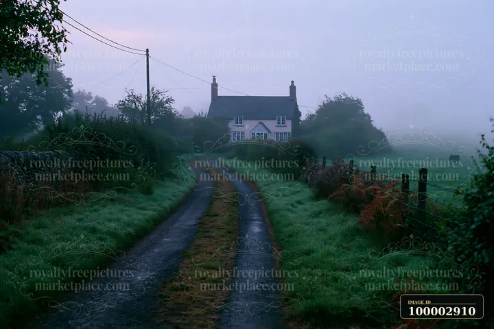 A cottage stands at the end of a dirt road in a misty countryside setting.