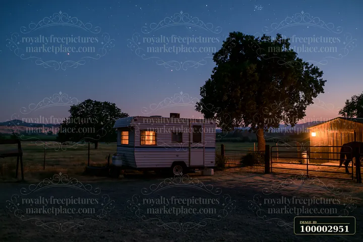 A horse trailer sits in a rural setting under a starry sky.