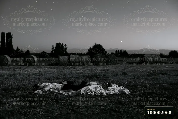 A couple lying on a blanket beneath stars in an open field during nighttime.