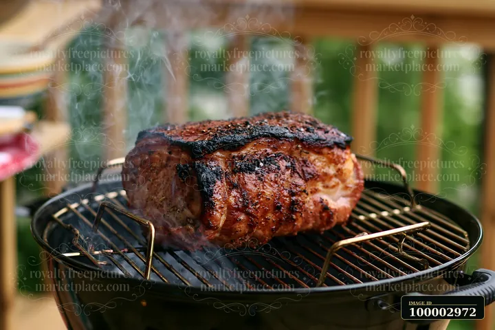 Smoke rises from a barbecue grill featuring a large roast pork.