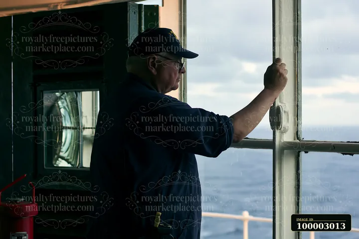 A lighthouse maintenance worker stands at a window, observing the view from the lighthouse tower.