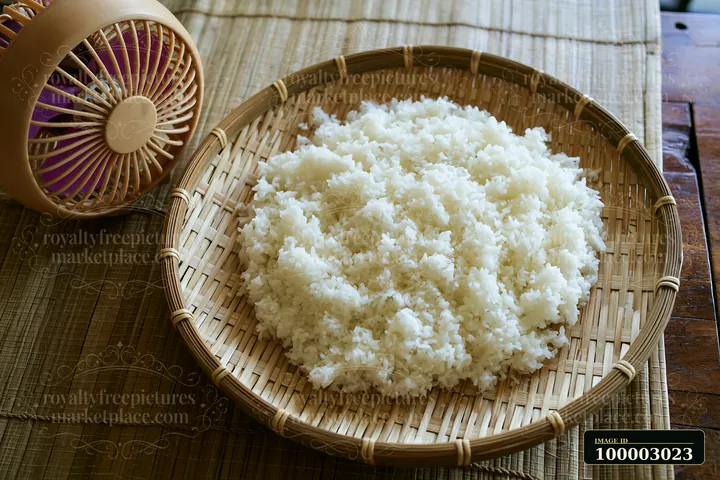 Sushi rice cooling on tray rests on a bamboo mat.