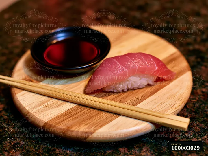 One nigiri beside soy sauce dish is served on a round wooden plate with chopsticks.