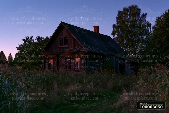 A wooden house stands surrounded by tall grass and trees as the blue hour sets in.
