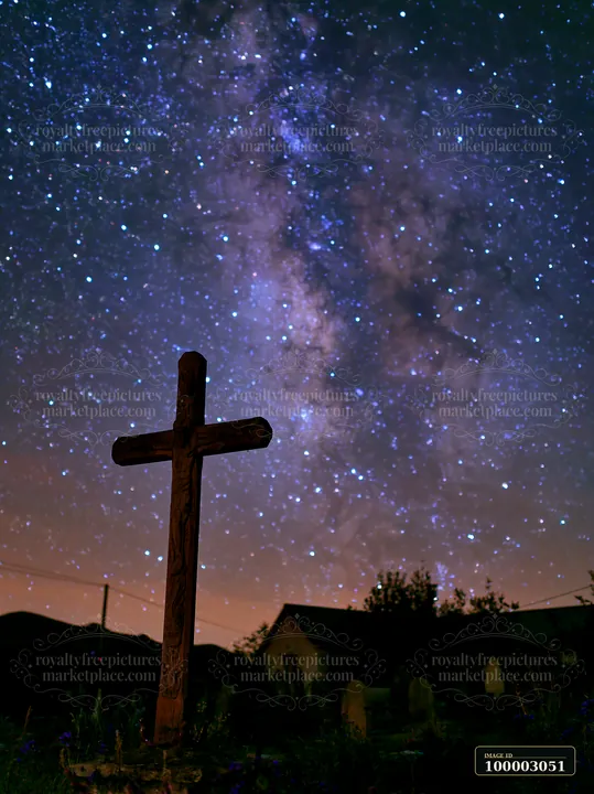 A wooden cross stands in a cemetery as the Milky Way galaxy fills the night sky.