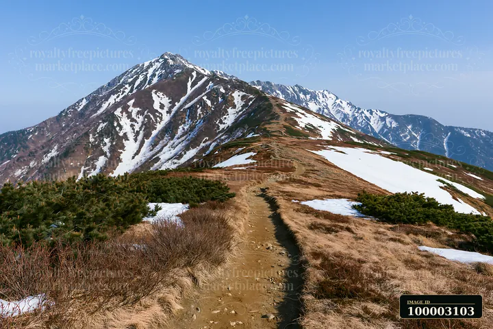 A hiking trail leads along a high mountain ridge with snow patches.