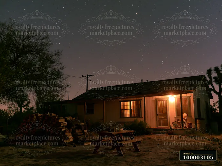 A desert home with a warm light glowing from the porch sits peacefully under a starry sky.