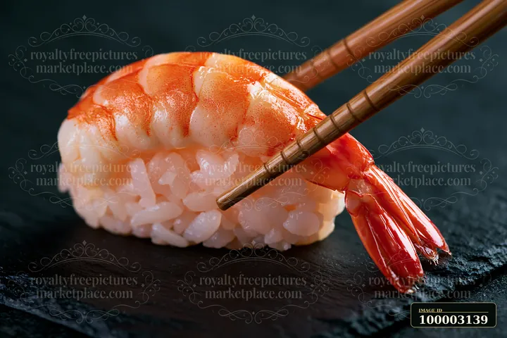 A single sushi piece with chopsticks is placed on a black stone plate.
