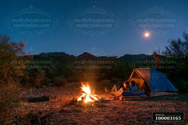 A couple sitting beside a glowing campfire under stars in a desert setting.