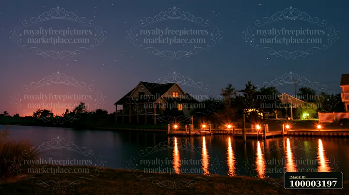 A coastal home overlooks the ocean horizon under a starry sky with visible lights reflecting in the water.